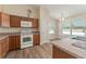 Bright kitchen with white appliances, wood cabinets, laminate counters, and view to eat-in area with natural light at 12054 Ne 51St Cir, Oxford, FL 34484