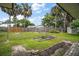 Fenced backyard featuring garden beds, grassy areas, and tall palm trees under a sunny sky at 1512 S Pointe Dr, Leesburg, FL 34748