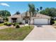 Charming home exterior featuring a two-car garage, manicured lawn, and lush tropical landscaping under a clear blue sky at 2461 Merida Cir, The Villages, FL 32162