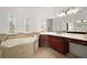 Bright bathroom featuring a soaking tub, tiled floors, wooden cabinets, and dual windows with decorative shutters at 38716 Oak Place Ct, Lady Lake, FL 32159
