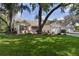 Attractive single-story home featuring a lush lawn, mature trees, and a brick-paved driveway to a two-car garage at 411 Loma Paseo Dr, The Villages, FL 32159