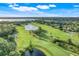 Expansive aerial view of the golf course, pond with fountain, and surrounding community with trees and green spaces at 9081 Saint Andrews Way, Mount Dora, FL 32757