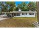 Front exterior featuring the home and car port, complemented by the front lawn, mature trees and blue sky at 1406 Spartan Ave, Leesburg, FL 34748