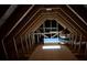 Exposed beams and wood frame in this unfinished attic space with insulation and bright light coming through the space at 16380 Se 83Rd Ct, Summerfield, FL 34491