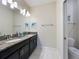 Bathroom featuring double sinks with dark cabinets, a granite countertop, and a toilet in a separate room at 9018 Stinger Dr, Davenport, FL 33896
