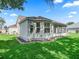 View of the home's back exterior featuring a screened in porch and manicured yard with lush green grass at 17427 Se 72Nd Overbrook Ct, The Villages, FL 32162