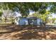 View of the fenced backyard with mature trees providing shade, and the blue exterior and roof of the property at 201 W Mirror Lake Dr, Fruitland Park, FL 34731