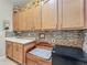 Bright laundry room with ample cabinet storage, mosaic tile backsplash, sink and adjacent tiled mudroom at 25523 Maurepas Ln, Leesburg, FL 34748