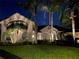An elegant home with lush landscaping, swaying palm trees, and illuminated features, glows against the backdrop of a twilight sky at 5530 Oxford Moor Blvd, Windermere, FL 34786