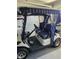Side view of a white golf cart with black seats and a blue striped canopy in a carpeted garage at 2063 Thornton Ter, The Villages, FL 32162