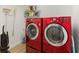 Laundry room with modern red washer and dryer units, complemented by storage shelves and cleaning supplies at 2403 Muirwood Pl, The Villages, FL 32162