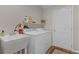 Functional laundry room with white appliances, sink, and storage shelf, perfect for organization and convenience at 2482 Ansley Path, The Villages, FL 32162