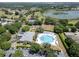 Aerial view of a community center featuring a large swimming pool, tennis courts, and lush greenery near a lake at 3723 Belle Rose Dr, Leesburg, FL 34748