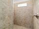 Walk-in shower featuring tan tiling, a window for natural light, and a shower head at 4972 Big Cypress St, Oxford, FL 34484