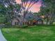 Charming home with manicured lawn, mature trees, and stone accents set against a colorful sunset sky at 2010 Otters Pond Rd, Fruitland Park, FL 34731
