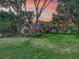 Charming home with manicured lawn, mature trees, and stone accents set against a colorful sunset sky at 2010 Otters Pond Rd, Fruitland Park, FL 34731