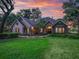 Charming home with manicured lawn, mature trees, and stone accents set against a colorful sunset sky at 2010 Otters Pond Rd, Fruitland Park, FL 34731