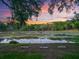 Scenic view of a tranquil pond covered in water lilies, framed by lush greenery and a colorful sunset sky at 2010 Otters Pond Rd, Fruitland Park, FL 34731