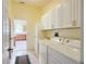 Practical laundry room with white appliances, cabinets, and a doorway to the kitchen at 3614 Auburndale Ave, The Villages, FL 32162