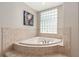 Corner bathtub surrounded by neutral tile and a window with glass blocks at 8715 Se 176Th Lowndes Pl, The Villages, FL 32162