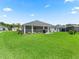 Expansive backyard featuring a screened-in patio, BBQ area, and ample green space surrounded by lush landscaping at 2006 Oppenheimer Ct, The Villages, FL 34762