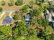 An aerial shot reveals a light blue home with a heart-shaped pool, nestled within a verdant, tree-filled landscape at 25541 Troon Ave, Sorrento, FL 32776
