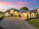Stunning home exterior boasts lush landscaping, a paver driveway, and a three-car garage beneath a colorful twilight sky at 39653 Grove Hts, Lady Lake, FL 32159