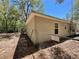 Side view of the house featuring tan siding, a chainlink fence, and glimpses of the surrounding wooded area at 40226 Palm St, Lady Lake, FL 32159