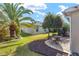 Landscaped backyard featuring lush green lawn, palm trees, and a stone patio at 857 Enisgrove Way, The Villages, FL 32163