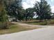 View of property entrance featuring a metal gate, gravel driveway, and a large shed with a lush tree backdrop at 7701 Groveland Farms Rd, Groveland, FL 34736