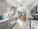 Modern kitchen with stainless steel dishwasher, light gray cabinetry, and tile floors, flowing into dining area at 919 Medira Dr, The Villages, FL 32159
