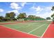Outdoor tennis court with a green playing surface and red border surrounded by a fence against a blue sky at 2112 Saint Ives Ct, Clermont, FL 34711