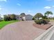 Wide view showing the circular brick driveway, mature landscaping, and a well maintained lawn at 3266 Woodridge Dr, The Villages, FL 32162