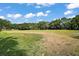 Wide open field with green and brown grass, backed by trees and a cloudy blue sky at 579 Juniper Way, Tavares, FL 32778