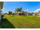 Expansive backyard with lush green lawn, mature palm trees and views of neighboring homes under a clear blue sky at 5818 Greenbriar Loop, Leesburg, FL 34788