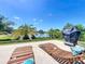 Relaxing backyard patio with lake view, lounge chairs, covered grill, and lush tropical landscaping at 8387 Bridgeport Bay Cir, Mount Dora, FL 32757