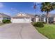 Daytime view of this property, featuring a three-car garage, manicured landscaping, and an American flag at 2124 Hames Ln, The Villages, FL 32162