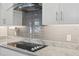 Modern kitchen featuring granite countertops, a glass cooktop stove, and stylish grey backsplash tiles at 395 S Dixie Dr, Howey In The Hills, FL 34737