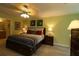 Cozy main bedroom featuring a ceiling fan, ensuite bath, and a king bed with wood frame and soft, neutral-toned bedding at 1482 Azteca Loop, The Villages, FL 32162