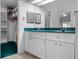 Bathroom with white cabinetry, teal countertop, mirrors, and an open closet with shelving on the left at 4547 Inverness Dr, Leesburg, FL 34748