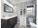 Nicely decorated bathroom with a navy blue vanity, floral wallpaper, and white storage cabinet at 8869 Se 159Th Pl, Summerfield, FL 34491