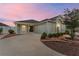 Inviting exterior view of home showcasing landscaping, attached garage and front door, as the sun sets at 9181 Se 166Th Sprung Ln, The Villages, FL 32162