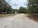 Wide shot of a home down a sandy drive with mature trees in a rural setting at 1203 High St, Wildwood, FL 34785