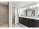 Bathroom with dual sinks, stylish dark cabinetry, and large tiled walk-in shower at 1309 Piney Woods Path, The Villages, FL 32163