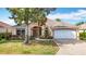 Charming single-story home featuring a lush front yard, arched entryway, and a brick paved driveway leading to a two-car garage at 2202 Kershaw Rd, The Villages, FL 32162