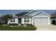 Charming single-story home with a manicured lawn, gray exterior paint, and a two-car garage at 6633 Holovak Ter, The Villages, FL 34762