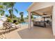 Covered patio area with outdoor furniture adjacent to a sparkling pool, waterfall, and lush landscaping at 2325 Kenya St, The Villages, FL 32162