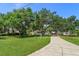 Long driveway leads to a charming white stucco home surrounded by mature trees and a lush lawn at 6750 Sunnyside Dr, Leesburg, FL 34748