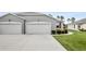 A modern one-story home with a gray exterior, two-car garage, and manicured lawn with bushes along the driveway at 27215 White Plains Way, Leesburg, FL 34748