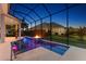 Screened-in pool with a fire feature, illuminated water, and lush landscaping at 4033 Swaying Palm Ct, The Villages, FL 32163